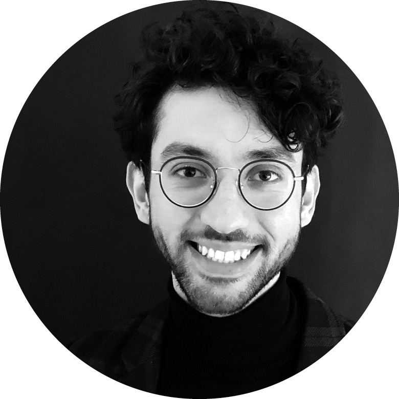 Porträt in schwarz weiß eines Mannes mit dunklen Haaren und Brille der in die Kamera lächelt