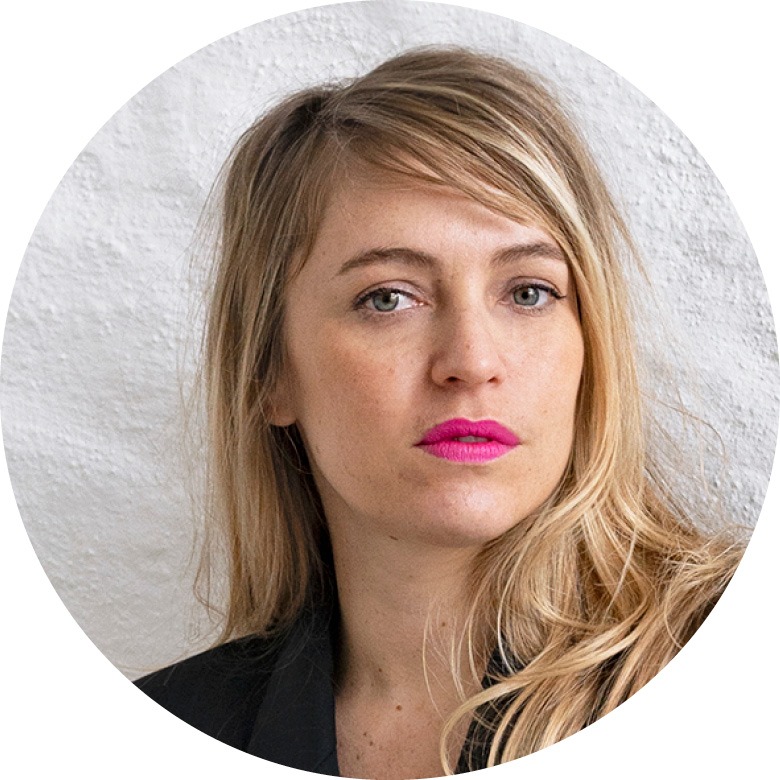 Frau mit blonden langen Haaren und pinkem Lippenstift schaut in die Kamera.