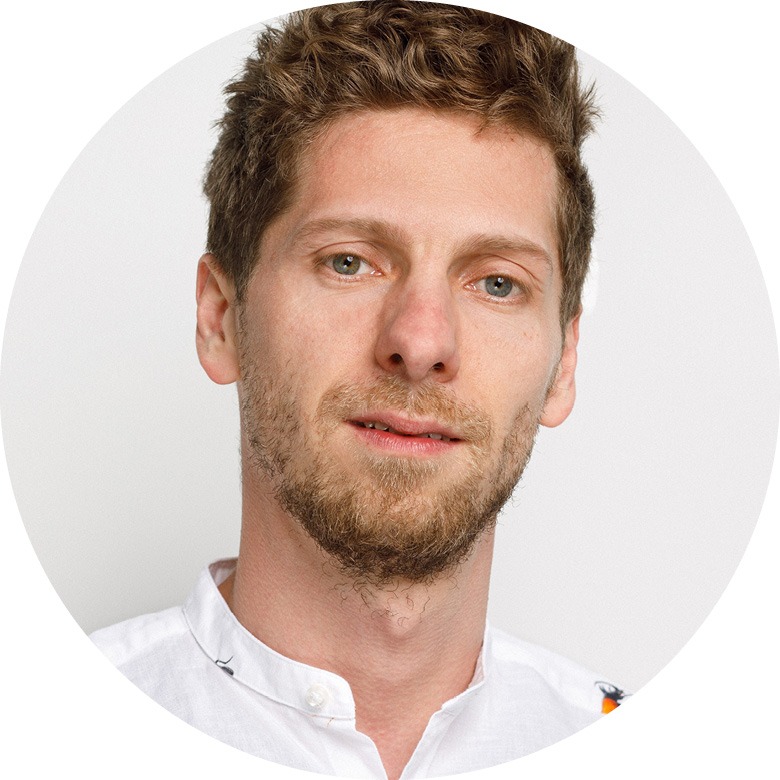 Mann mit kurzen dunkelblonden Haaren und Dreitagebart. Er trögt ein weißes Hemd und schaut in die Kamera.