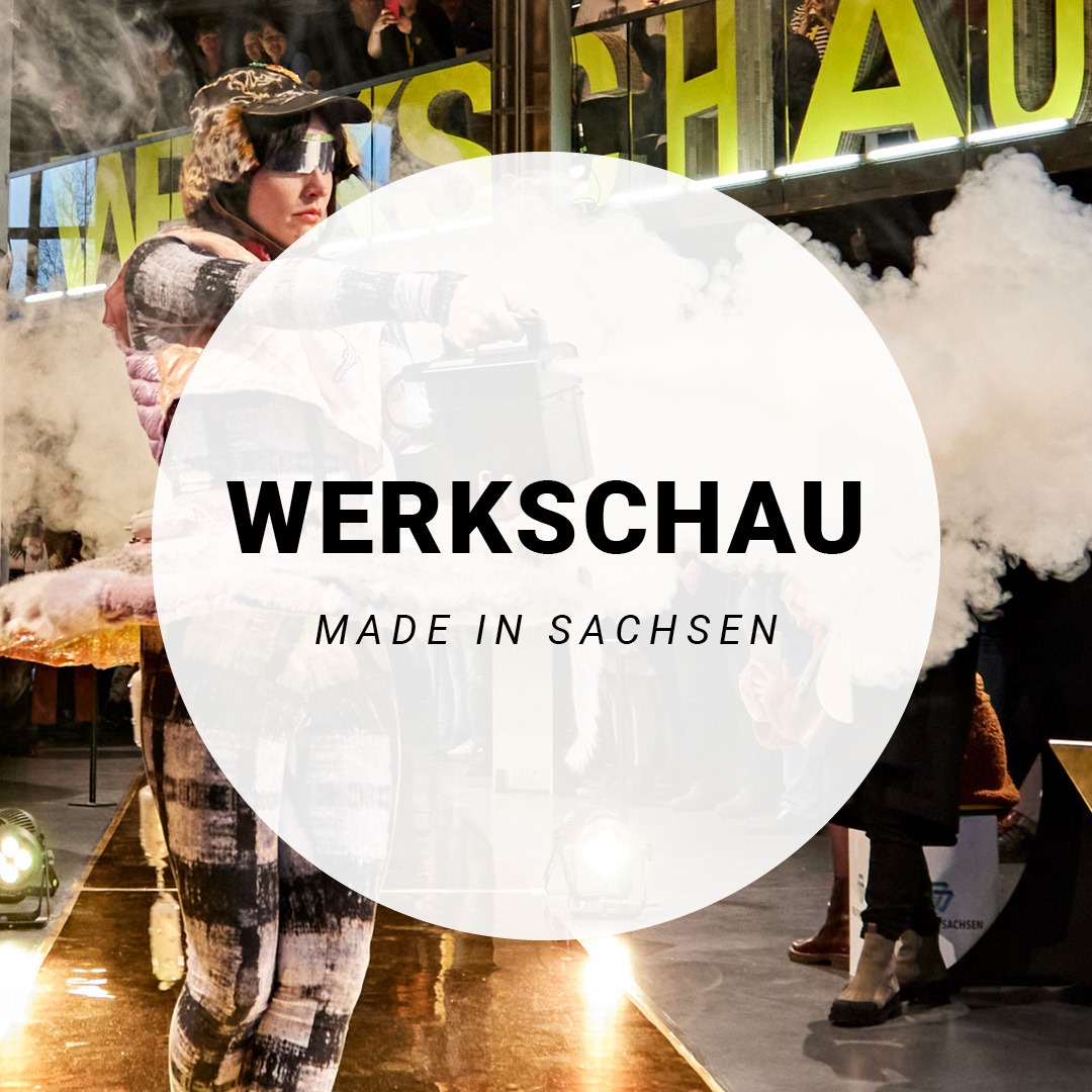 Eine Bühne mit einer Person in Kostüm darauf, im Vordergrund ein weißer Kreis mit der Aufschrift: Werkschau. Made in Sachsen.